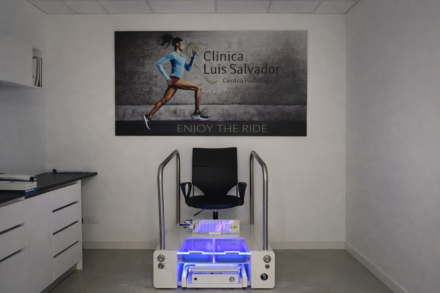 Estudio de la pisada con plataforma de presiones en clínica de podología moderna en Valencia, con equipo biomecánico iluminado y entorno sanitario profesional.